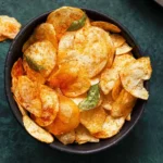 A bowl of spicy chips garnished with chili flakes and served with a side of dipping sauce.