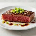 Seared ahi tuna slices with a perfectly crusted exterior, served on a plate with a side of greens and dipping sauce