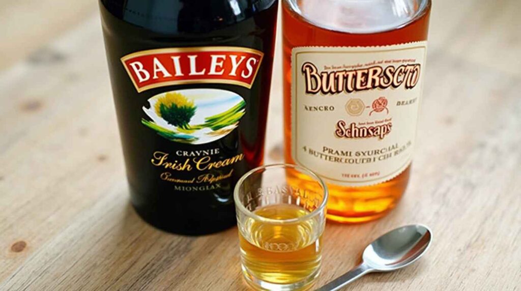 Ingredients for a buttery nipple cocktail, including butterscotch schnapps, Irish cream, and a shot glass on a sleek countertop.