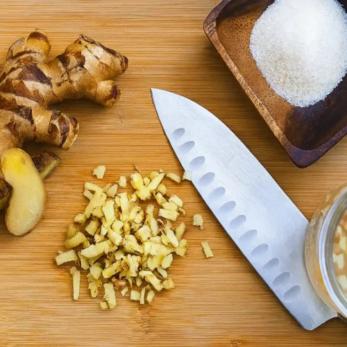 Person holding spoon of fizzy ginger bug with ingredients on table