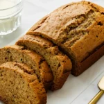Freshly baked zucchini bread loaf sliced on a marble counter with butter and milk.