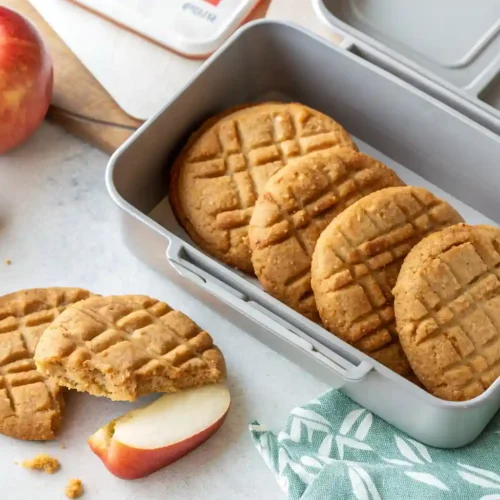 Chewy peanut butter cookies with a fork pattern being placed into a school lunchbox with a red apple.Best Back to School Cookies