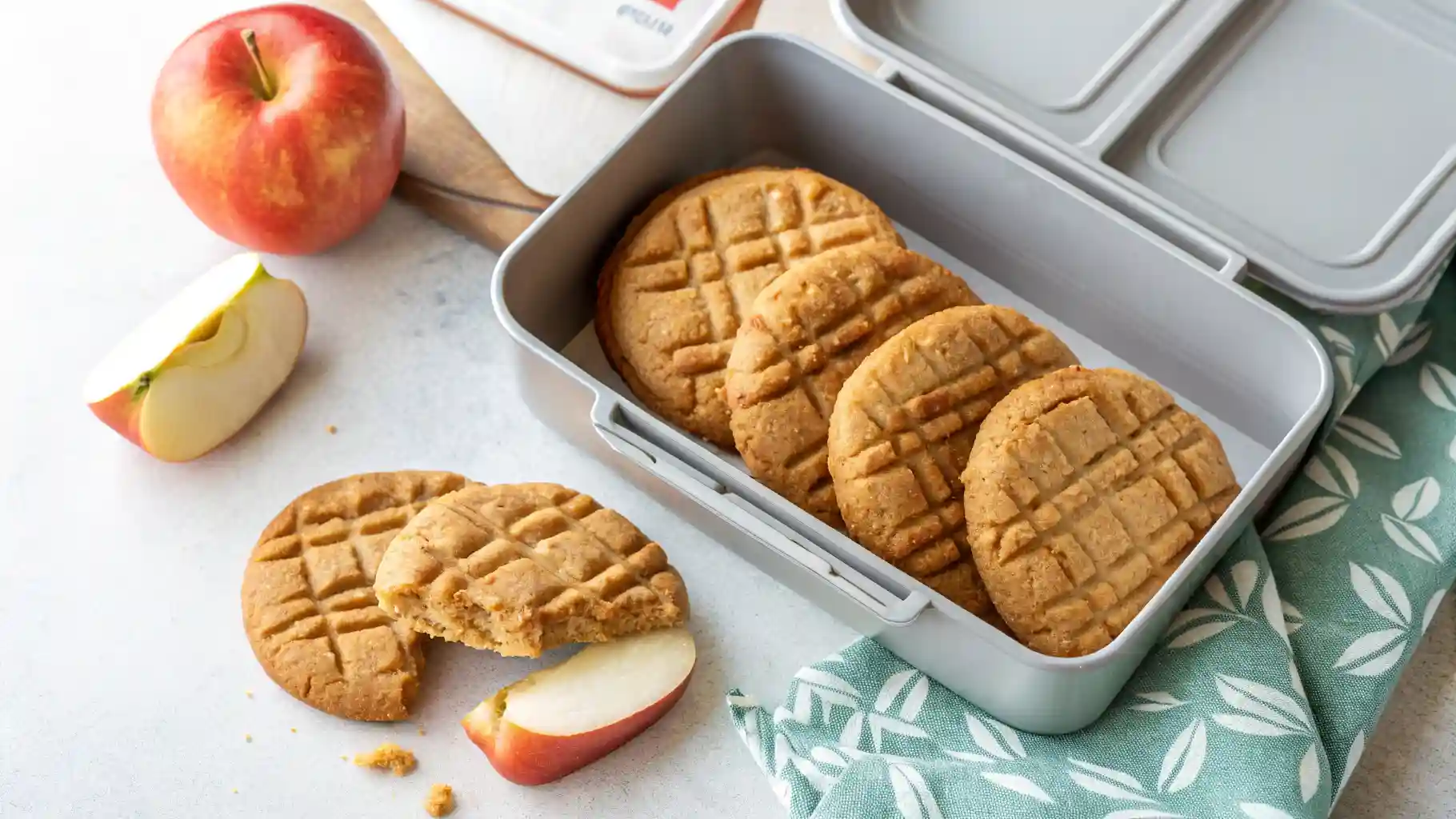 Chewy peanut butter cookies with a fork pattern being placed into a school lunchbox with a red apple.Best Back to School Cookies