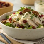 "A vibrant, creamy deli-style turkey salad in a rustic off-white ceramic bowl, garnished with whole dried cranberries, chopped walnuts, and fresh tarragon sprigs. A silver serving spoon rests in the bowl, which is placed on a light wooden surface beside a white linen napkin. The image is a close-up, soft-focus shot highlighting the salad's texture and ingredients."
