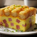 A perfect slice of crispy tater tot breakfast casserole on a white plate, showing fluffy eggs and a golden-brown top.