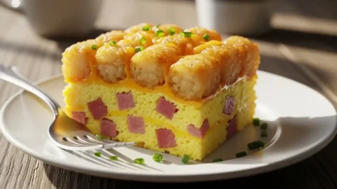 A perfect slice of crispy tater tot breakfast casserole on a white plate, showing fluffy eggs and a golden-brown top.
