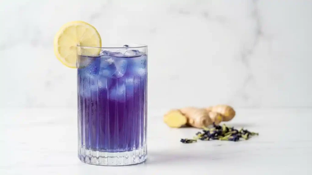 Elegant glass of vibrant blue-purple ACV tonic with lemon garnish on a white marble surface, ready for consumption.