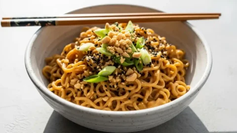 A large bowl of Healthy Peanut Butter Ramen Noodles garnished with crushed peanuts, green onions, and sesame seeds, ready to eat.