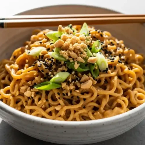 A large bowl of Healthy Peanut Butter Ramen Noodles garnished with crushed peanuts, green onions, and sesame seeds, ready to eat.