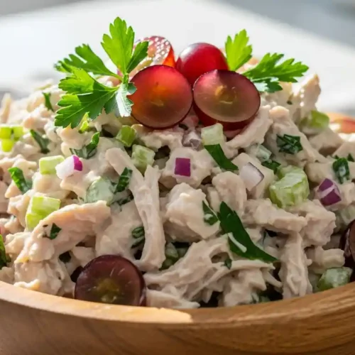 Close-up of creamy high protein chicken salad with grapes and parsley in a wooden bowl on a light tablecloth.