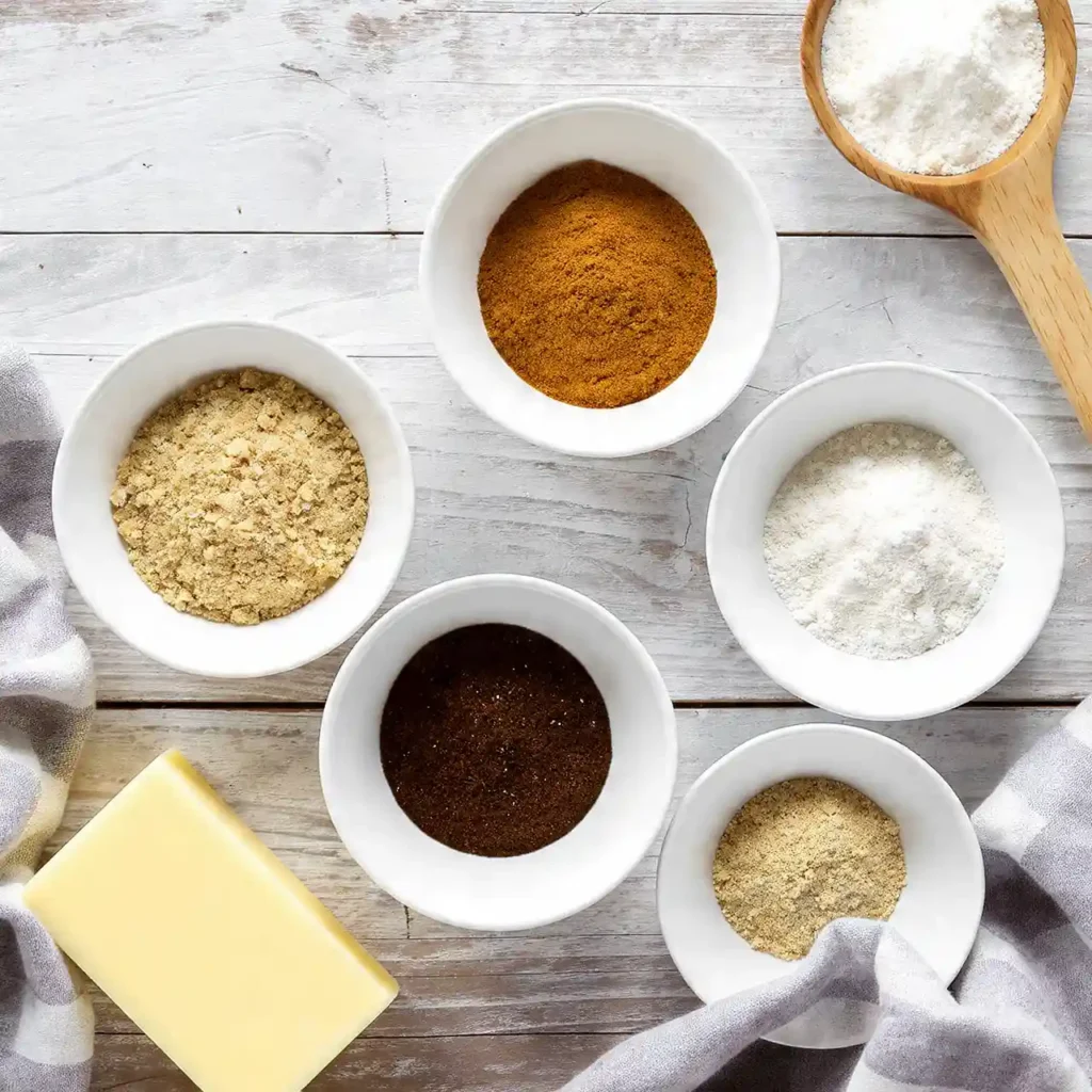 Flat lay of cinnamon knot ingredients including flour, brown sugar, cinnamon, instant coffee, and powdered sugar, organized in white bowls.