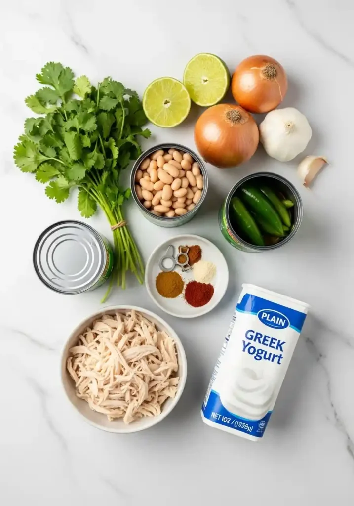 Overhead flat-lay view of all ingredients required to make high protein white chicken chili, including shredded chicken, canned beans, spices, and Greek yogurt.