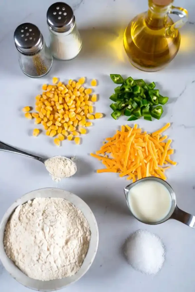 Overhead view of all fresh ingredients for jalapeno corn nuggets laid out on a marble surface.