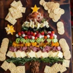 A beautiful Christmas tree-shaped charcuterie board overflowing with meats, cheeses, fruits, and olives, garnished with rosemary and a cheese star.