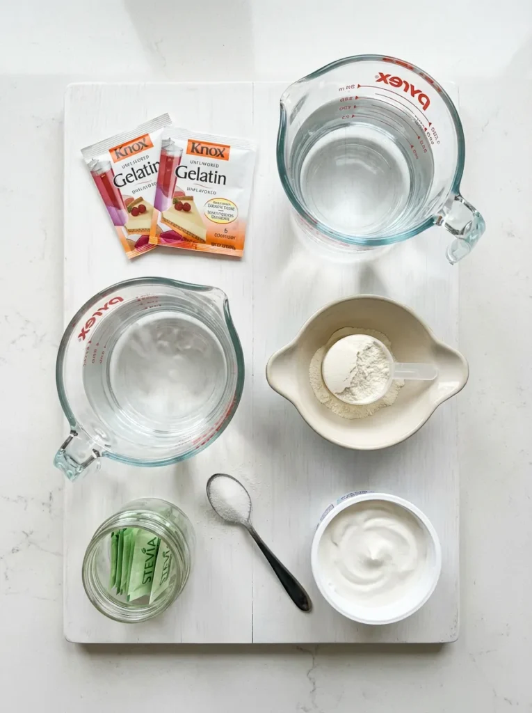 Flat lay of bariatric gelatin ingredients: gelatin packets, measuring cups with water, whey protein powder, and optional sweetener and whipped topping.