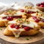 Close-up of freshly made Cranberry Brie Pear Crostini on a wooden board, garnished with thyme, ready to serve.