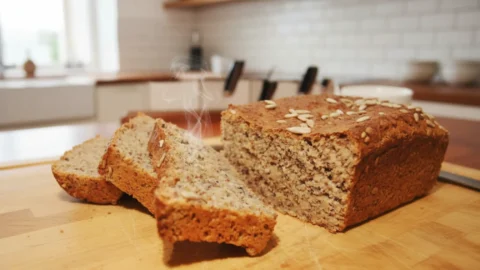A golden-brown loaf of homemade Ezekiel bread on a wooden cutting board with several slices cut, revealing its dense, wholesome crumb.