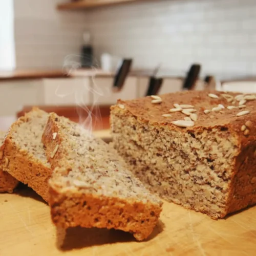 A golden-brown loaf of homemade Ezekiel bread on a wooden cutting board with several slices cut, revealing its dense, wholesome crumb.