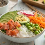 Overhead shot of a colorful and fresh salmon avocado poke bowl with sushi rice, marinated salmon, avocado, edamame, cucumber, mango, and sesame seeds.