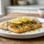 Close-up of a beautifully baked steelhead trout fillet garnished with fresh dill and lemon slices on a white plate.