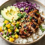 A vibrant and healthy coconut chicken rice bowl with fresh mango salsa, avocado, and grilled chicken on a bright table.