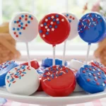 A platter of red, white, and blue chocolate-dipped Oreo cookies on sticks with patriotic sprinkles.