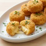 Close-up of crispy, golden-brown smoked gouda mac and cheese bites on a white platter with one bite showing a creamy interior.