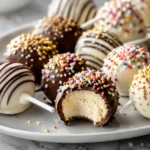 A variety of chocolate-dipped frozen cheesecake pops on sticks, decorated with sprinkles and displayed on a white platter.