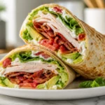 A close-up of a Turkey Club Wrap sliced in half, showing layers of turkey, bacon, avocado, and lettuce.