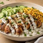 A professionally styled chicken rice bowl with sliced seared chicken, jasmine rice, cucumbers, corn, and a creamy drizzle on a wooden table.