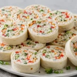 A close-up shot of several colorful veggie pinwheels featuring cream cheese, ranch seasoning, and fresh vegetables rolled in flour tortillas.