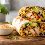 A close-up of a Southwest Chicken Wrap cut in half, showing layers of seasoned chicken, black beans, corn, and avocado.