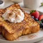Golden brown French toast with whipped cream, cinnamon, and fresh berries