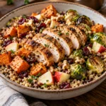 A warm and inviting autumn harvest bowl filled with roasted sweet potatoes, Brussels sprouts, chopped apple, walnuts, and cranberries, topped with sliced cooked chicken breast.