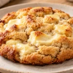 A freshly baked cheesecake cookie with golden brown edges and a melted texture