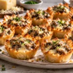 A platter of golden-brown mini phyllo tartlets filled with a savory sautéed mushroom and melted cheese mixture, garnished with fresh chives.