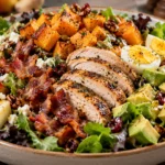 A large bowl of harvest salad with mixed greens, roasted butternut squash, crispy turkey bacon, sliced chicken, hard-boiled eggs, diced apple, and diced avocado.