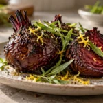 A dish of roasted beets, garnished with fresh tarragon and lemon zest, on a light wood kitchen table